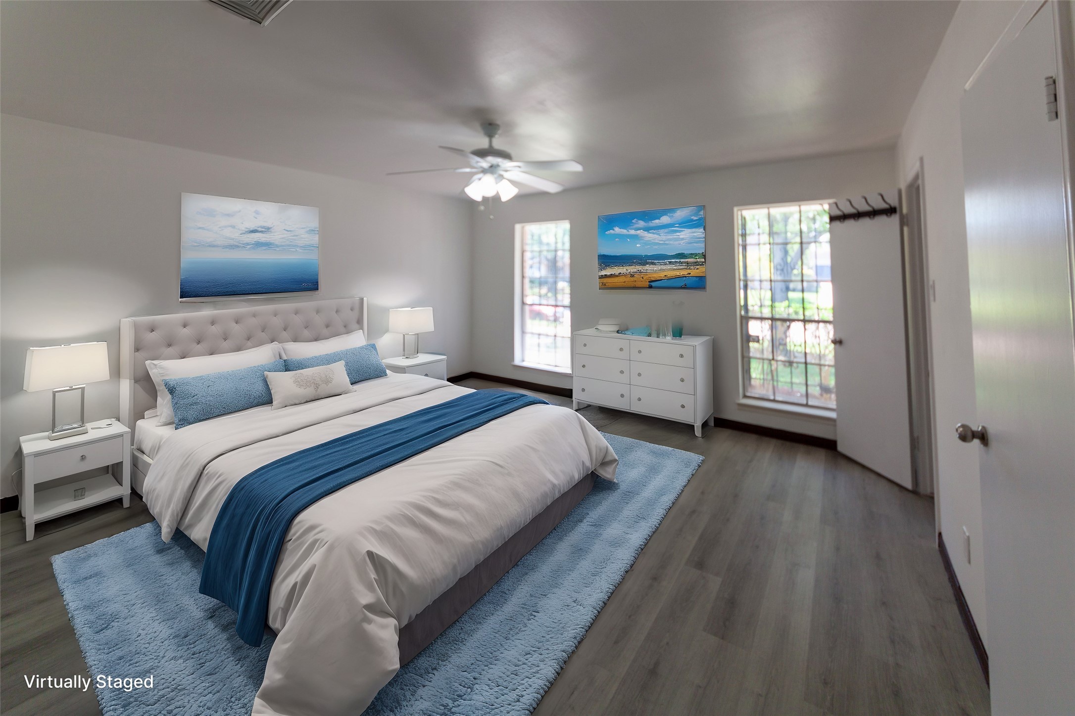 8826 Roos Road Houston, TX 77036 - Photo 15 of 42 Bright, spacious bedroom with modern flooring, large windows, and ceiling fan. Features a cozy bed with blue accents, two nightstands, and a dresser. Decorated with calming ocean-themed artwork.