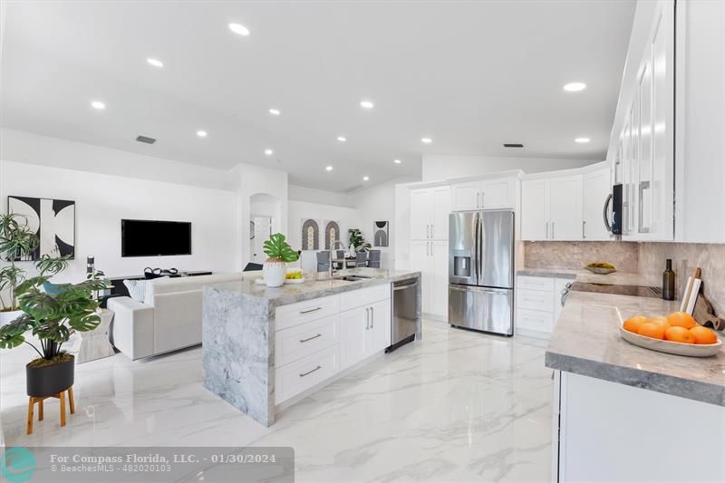 a large white kitchen with stainless steel appliances granite countertop a couch and a stove top oven