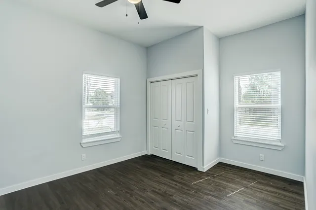 an empty room with wooden floor chandelier fan and windows