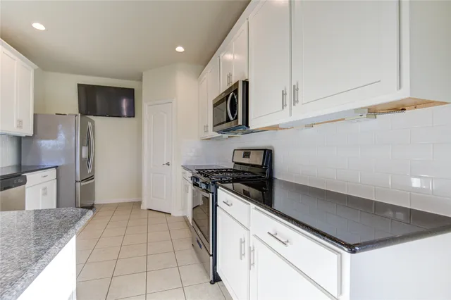 a kitchen with stainless steel appliances granite countertop white cabinets a stove top oven a sink and dishwasher