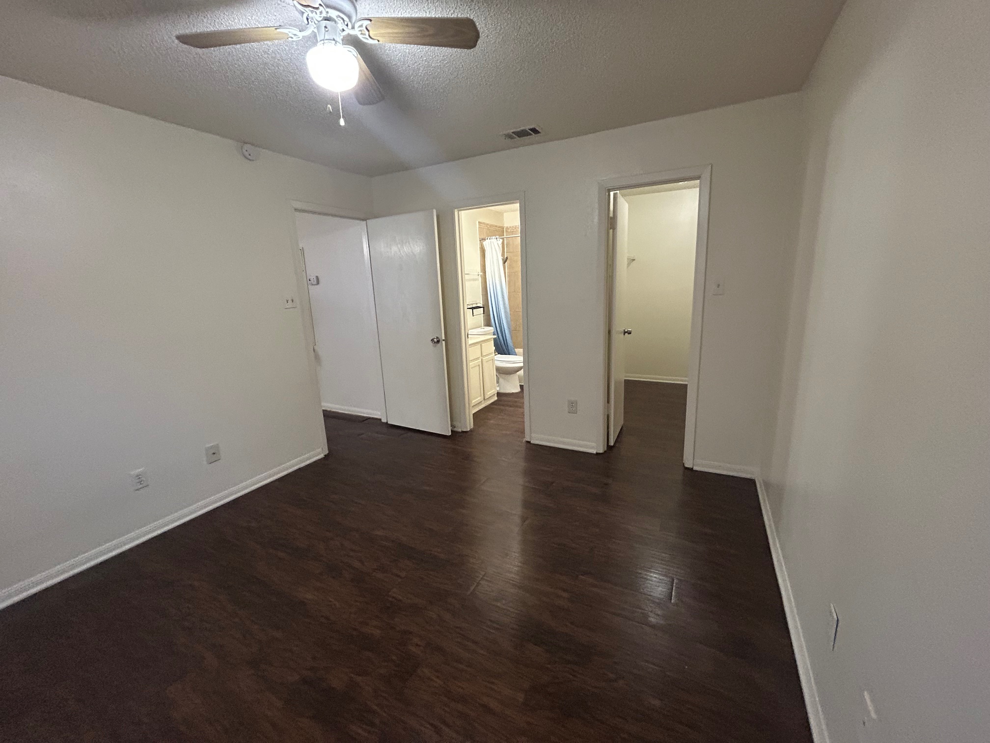 8812 Schick Road, Unit C Austin, TX 78729 - Photo 12 of 12 Unfurnished bedroom featuring a textured ceiling, dark wood-style floors, a spacious closet, a ceiling fan, and connected bathroom