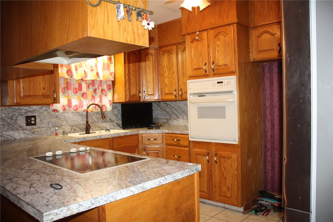 402 Canaan Road Marshall, AR 72650 - Photo 12 of 37 Kitchen featuring wood cabinetry, light-toned countertops, a built-in electric cooktop, a wall oven, and a single basin sink with a gooseneck faucet