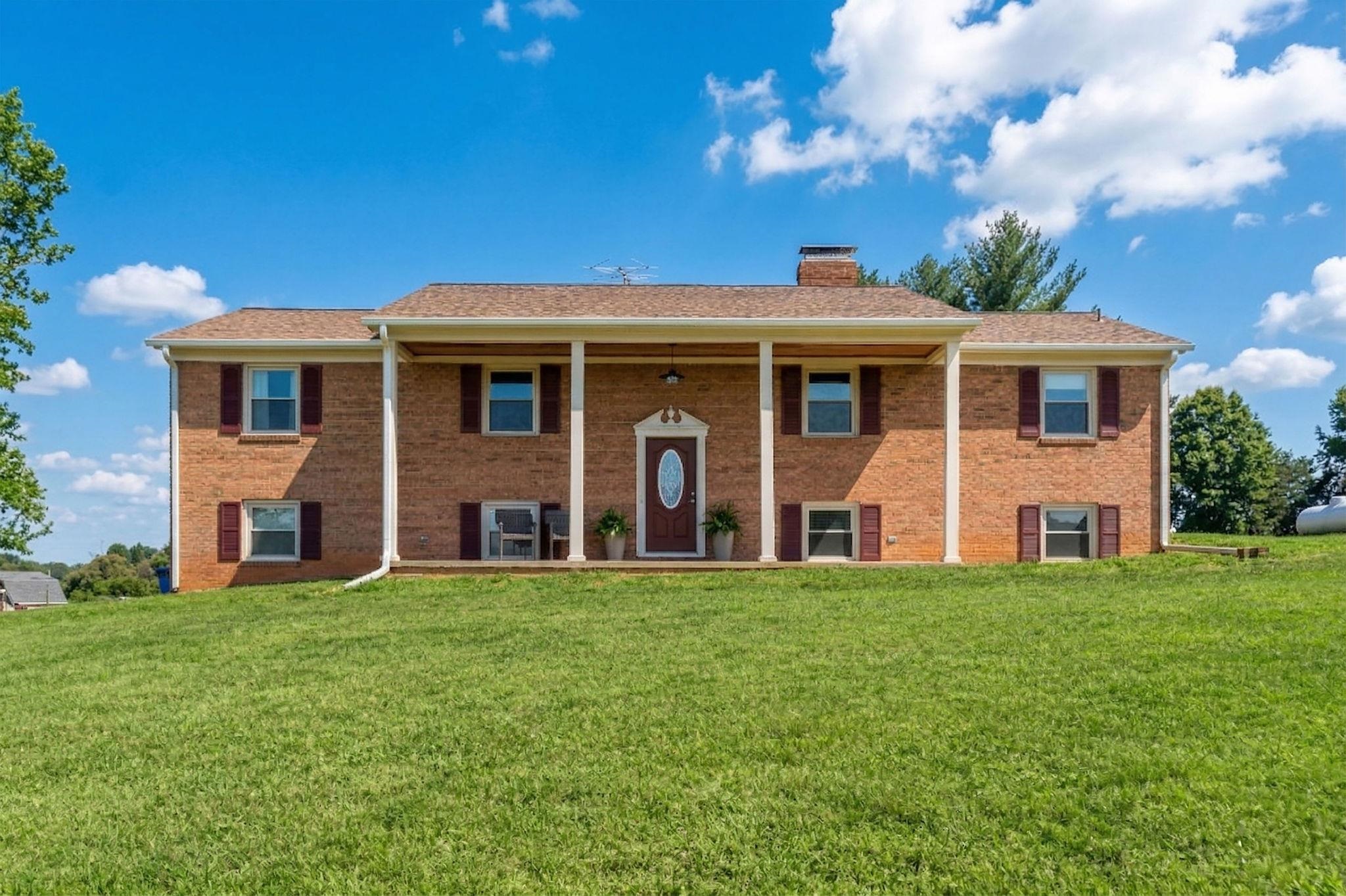 a view of a brick house with a big yard and large trees