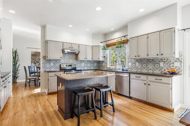 a kitchen with stainless steel appliances granite countertop a stove top oven a sink dishwasher a dining table and chairs with wooden floor