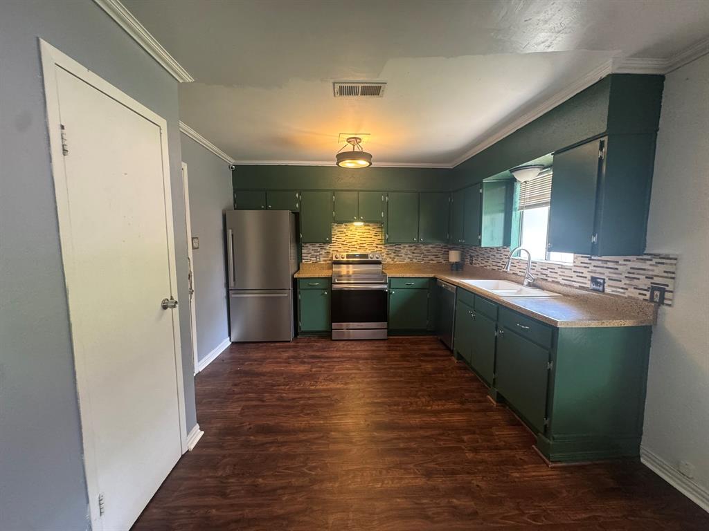 812 Reveille Road Fort Worth, TX 76108 - Photo 3 of 22 Kitchen featuring wood-finish flooring, dark green cabinetry, light-toned countertops, a mosaic tile backsplash, and stainless steel appliances