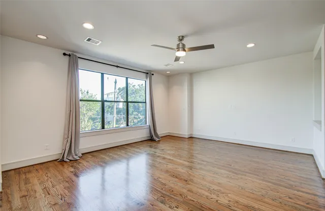 an empty room with wooden floor fan and windows
