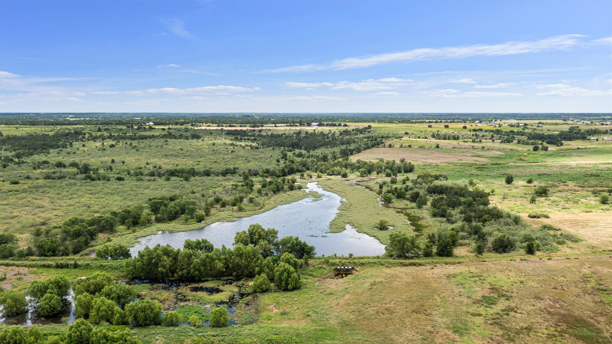 3315 County Road 463 Elgin, TX 78621 - Photo 16 of 32 Vast, open terrain offers a serene lake amidst abundant greenery under a clear sky.