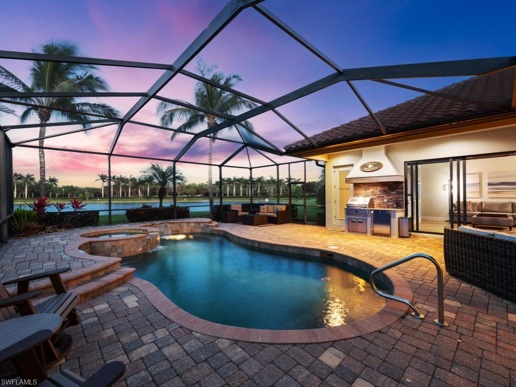 9430 Italia Way Naples, FL 34113 - Photo 3 of 47 Pool at dusk featuring outdoor lounge area, an outdoor kitchen, a pool with connected hot tub, and a patio area