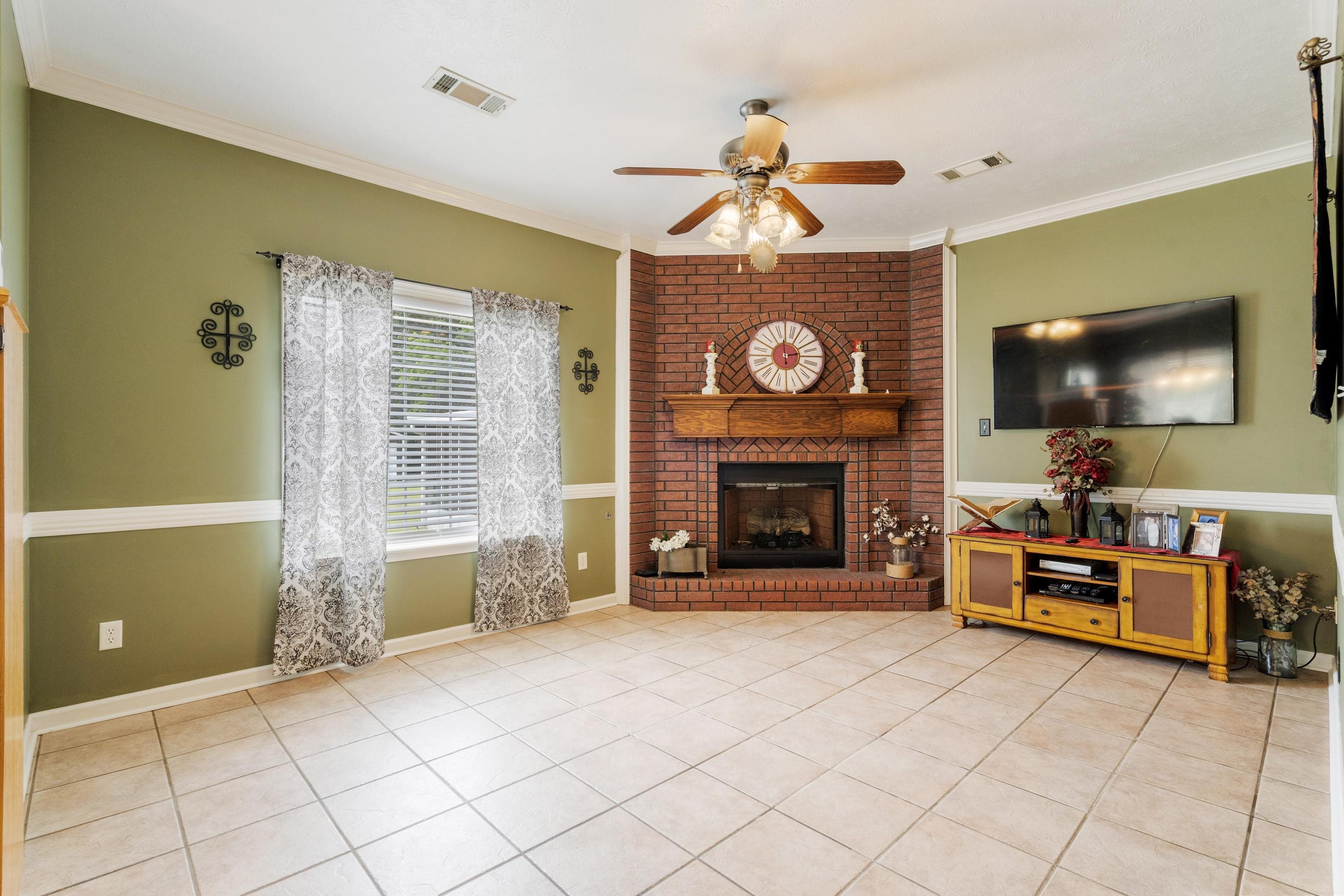7757 Brunswick Road Millington, TN 38053 - Photo 9 of 40 Living area featuring a corner brick fireplace with a wood mantel, tile flooring, crown molding, and a ceiling fan with integrated lighting