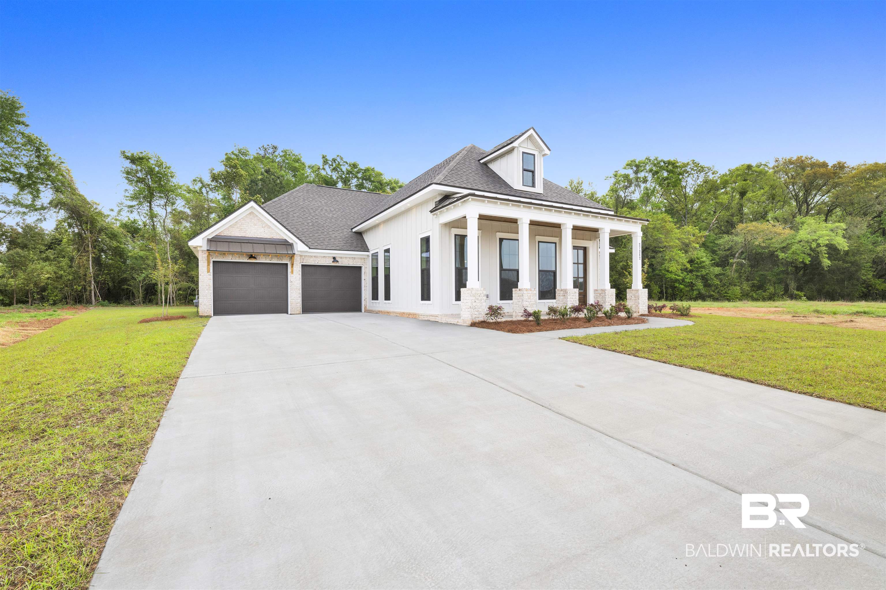 Modern farmhouse with a front lawn, a porch, an attached garage, and driveway