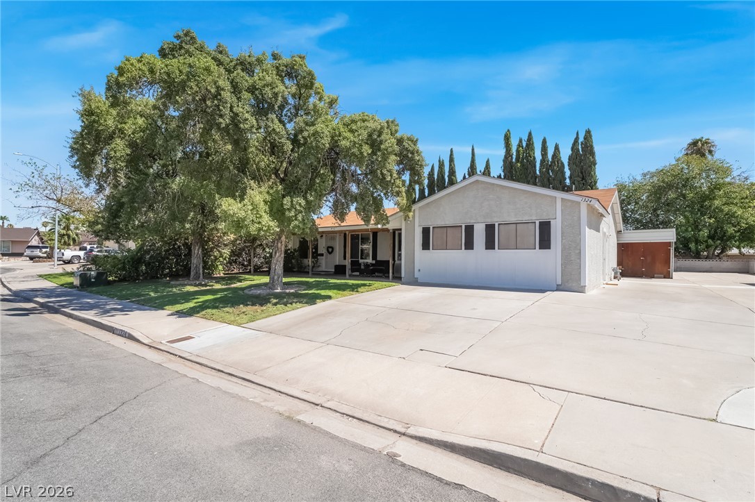 Mature trees frame a wide concrete driveway leading to the low-profile suburban exterior.