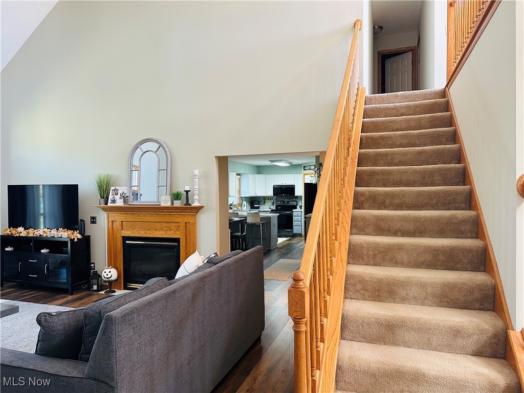 2435 Queensbury Road Alliance, OH 44601 - Photo 15 of 36 Living area featuring a glass covered fireplace, stairs, wood finished floors, and a towering ceiling