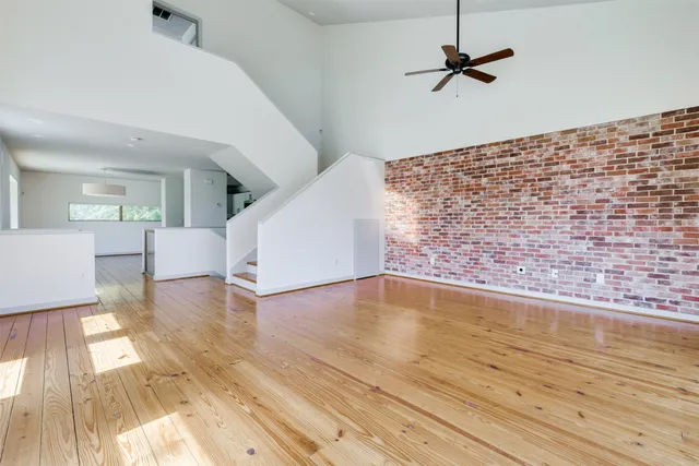 an empty room with wooden floor fan and windows
