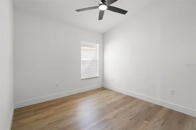 an empty room with wooden floor fan and windows