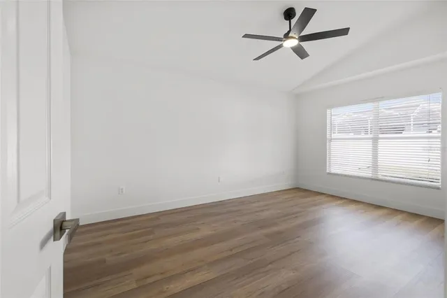 an empty room with wooden floor fan and windows