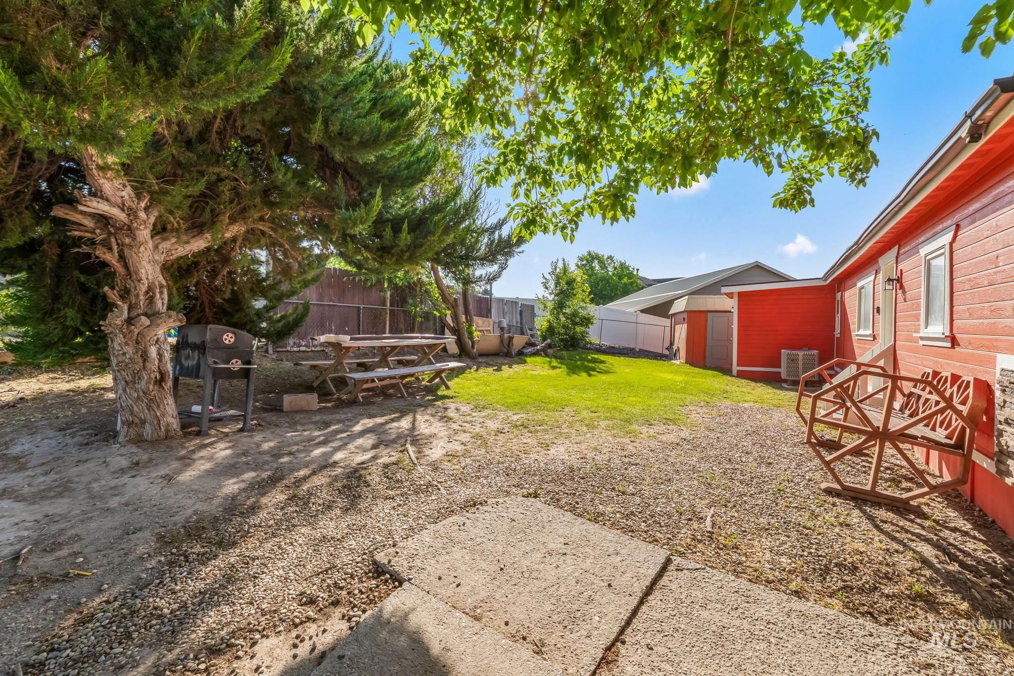20106 Lower Pleasant Ridge Road, Unit 29 Caldwell, ID 83607 - Photo 3 of 19 Expansive backyard featuring a large tree, a grass lawn, and a red exterior property