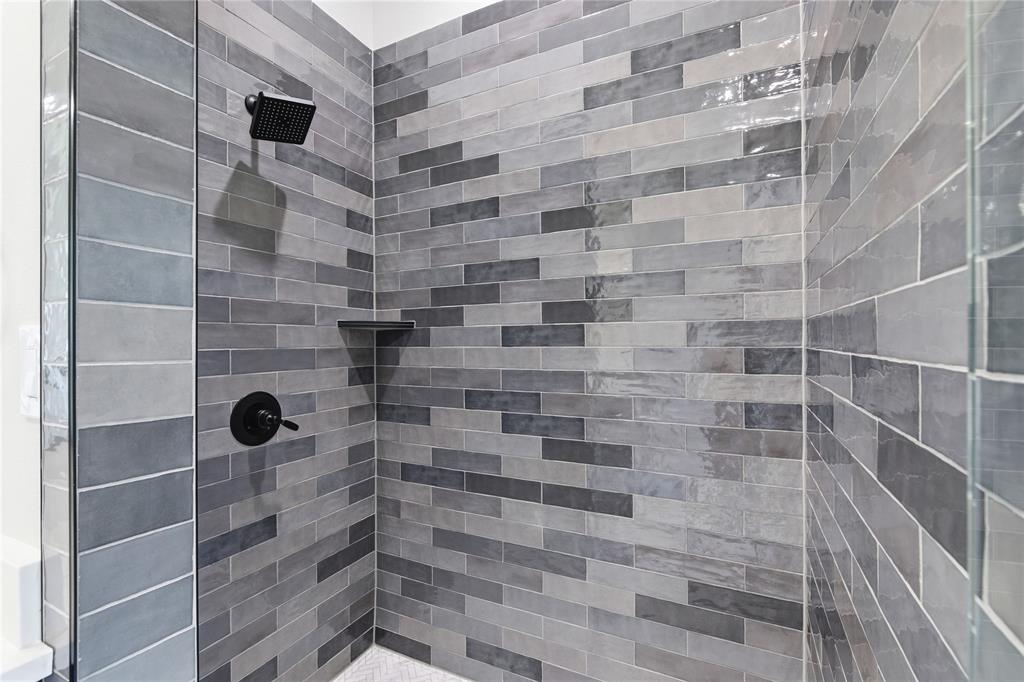 713 Anne Road Van Alstyne, TX 75495 - Photo 13 of 29 Shower enclosure featuring variegated grey tile walls, a matte black rain shower head, coordinating matte black shower controls, a built-in shower shelf, and a glass partition