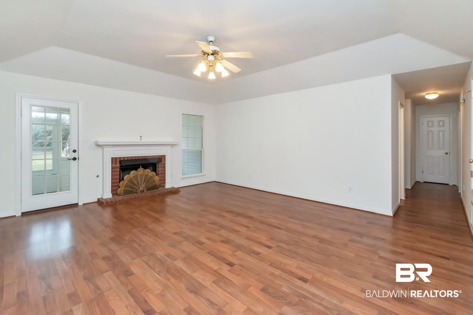 10006 Wedgefield Court Mobile, AL 36608 - Photo 21 of 34 Unfurnished living room featuring a brick fireplace, baseboards, a ceiling fan, and wood finished floors