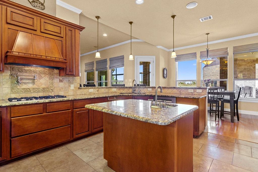 117 Citation Drive Cresson, TX 76035 - Photo 15 of 40 Kitchen with brown cabinets, pendant lighting, ornamental molding, a peninsula, and light stone counters