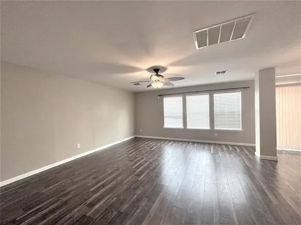 a view of an empty room with wooden floor and a kitchen