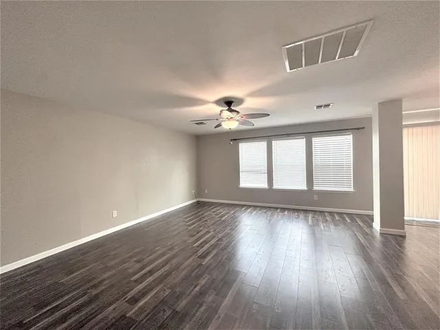 a view of an empty room with wooden floor and a kitchen