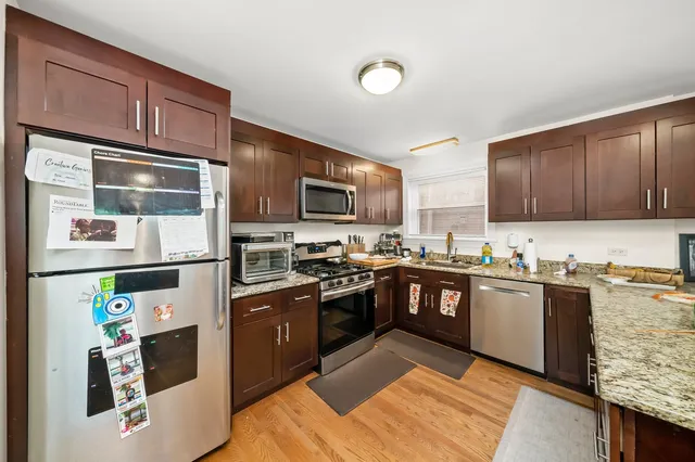 a kitchen with stainless steel appliances granite countertop a stove top oven a sink dishwasher and a refrigerator with wooden cabinets