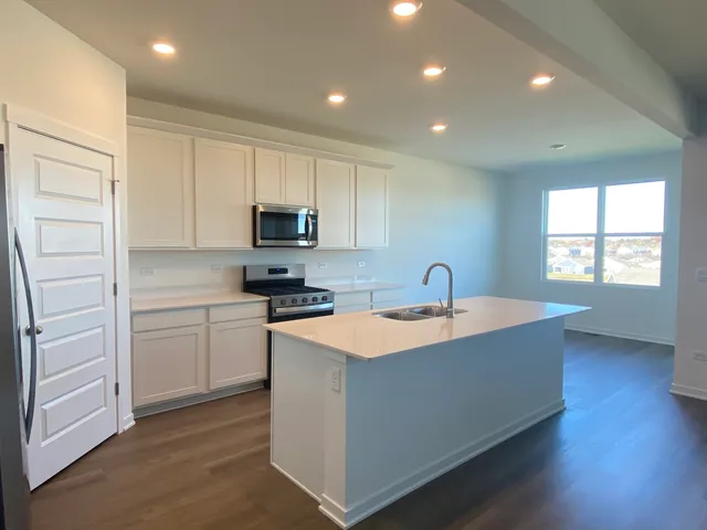 a kitchen with stainless steel appliances granite countertop a sink dishwasher a stove and a refrigerator with wooden floor