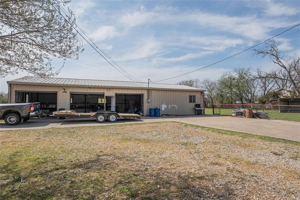 900 Silver Creek Azle Road Azle, TX 76020 - Photo 19 of 27 Metal-sided workshop with a light-colored metal roof, two roll-up garage doors, a side entry door, and a built-in outdoor sink