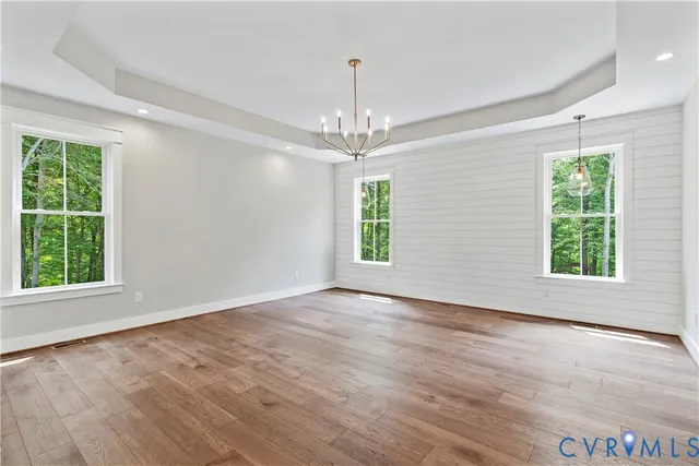 an empty room with wooden floor chandelier and windows