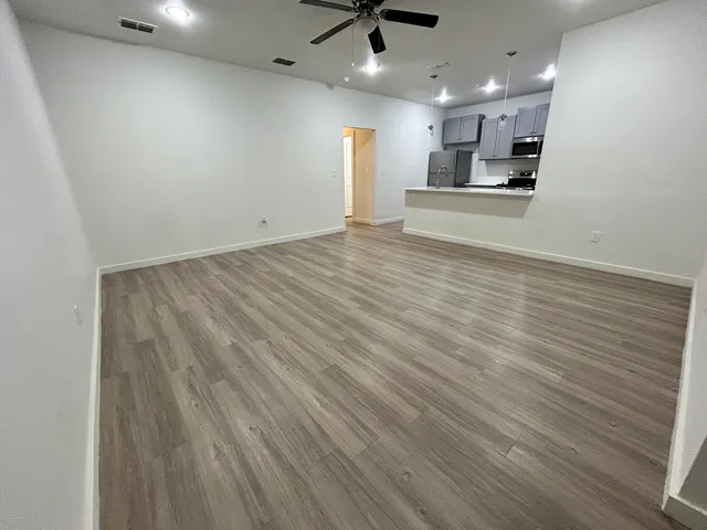 an empty room with wooden floor kitchen view and windows