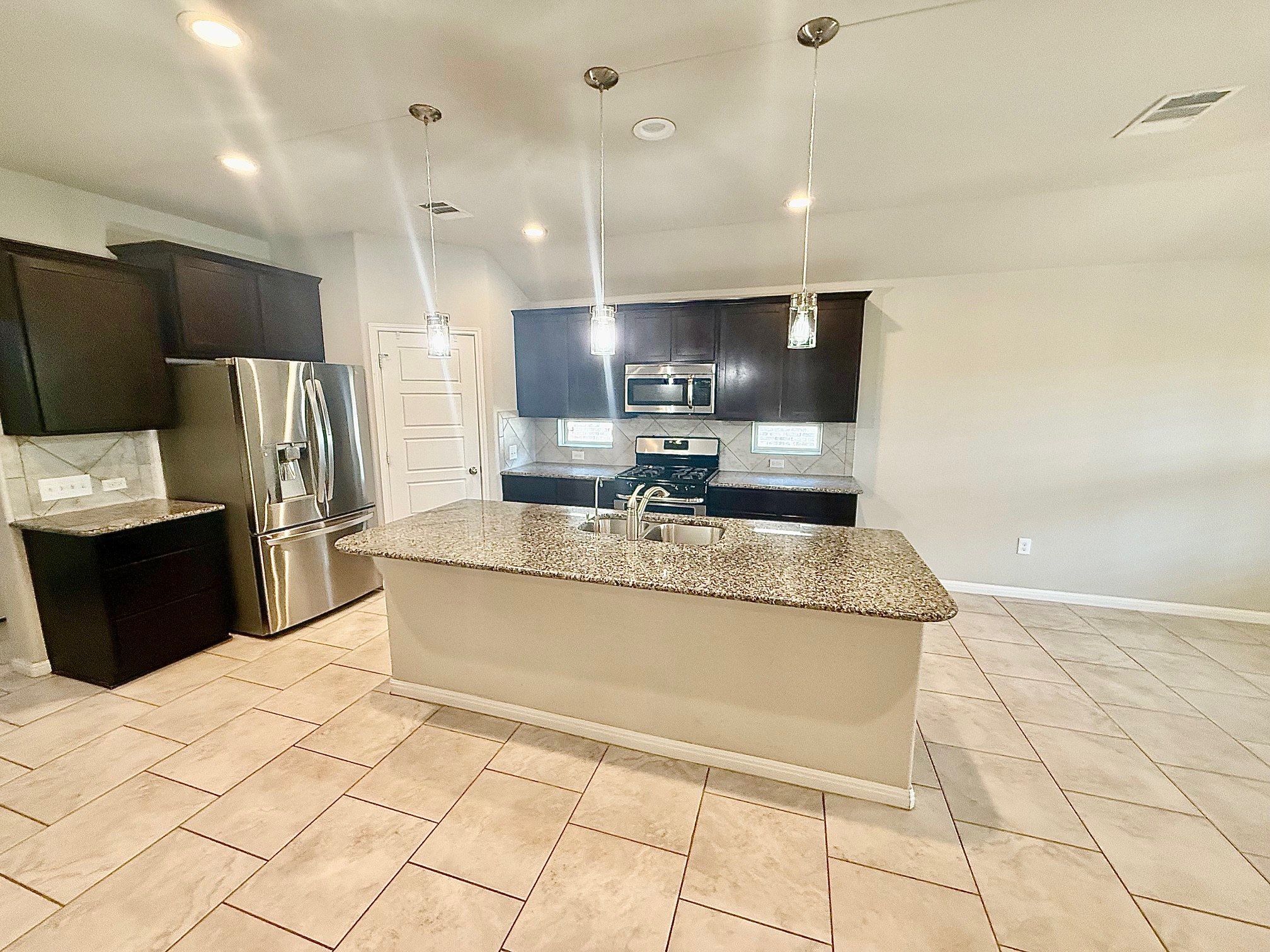 513 Longhorn Cavern Road Leander, TX 78641 - Photo 4 of 24 Kitchen with stainless steel appliances, light stone counters, decorative backsplash, a kitchen island with sink, and decorative light fixtures