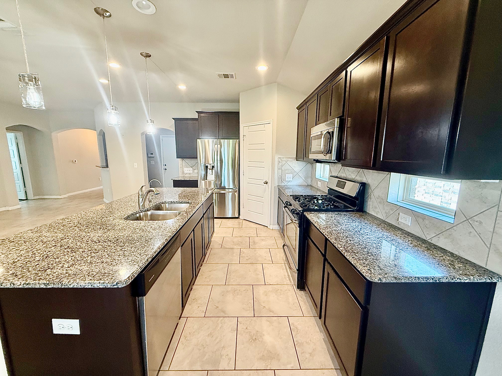 513 Longhorn Cavern Road Leander, TX 78641 - Photo 5 of 24 Kitchen with arched walkways, stainless steel appliances, dark wood finish cabinetry, decorative backsplash, and light stone countertops
