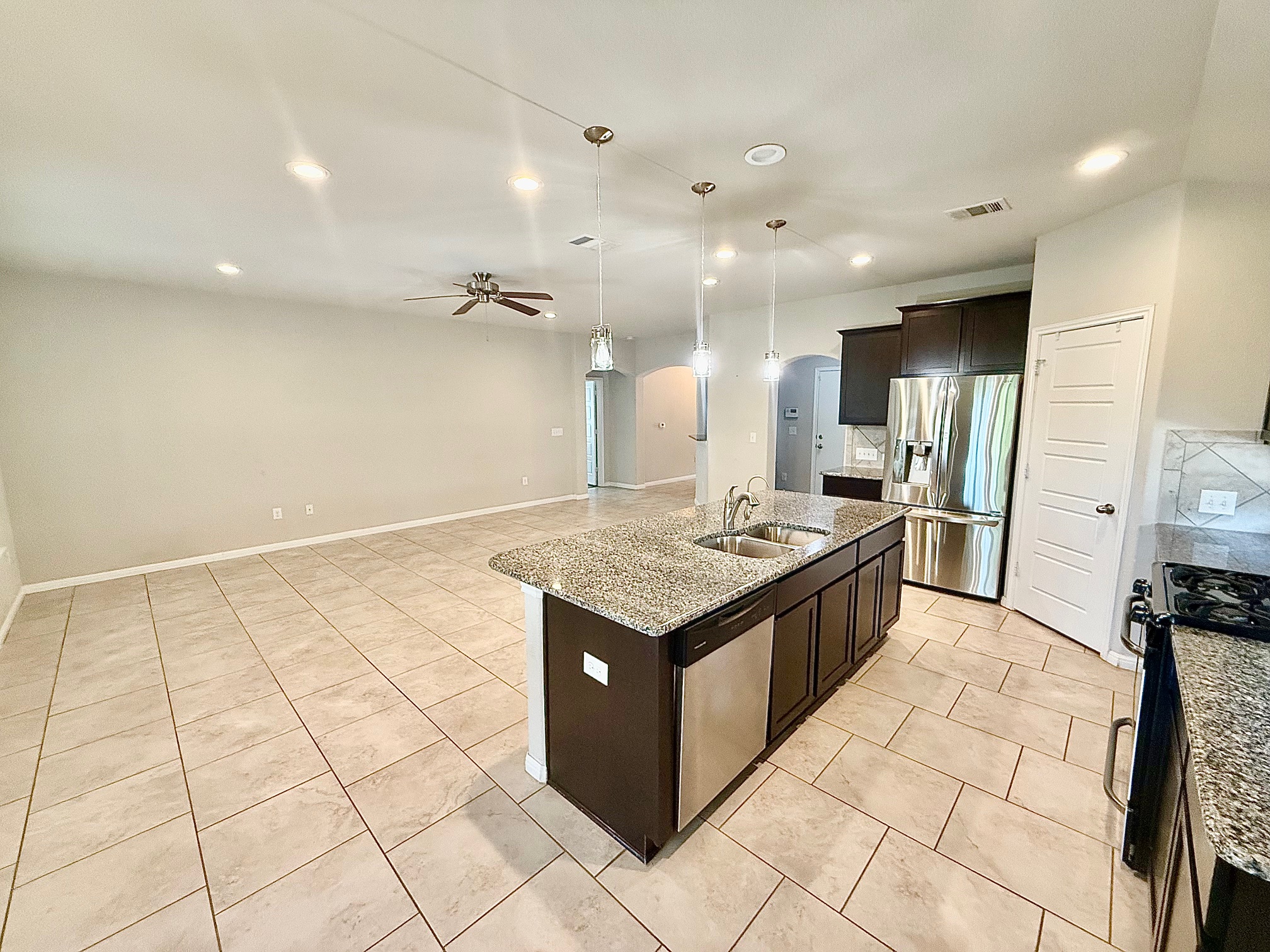 513 Longhorn Cavern Road Leander, TX 78641 - Photo 6 of 24 Kitchen with dark wood finish cabinetry, light stone countertops, arched walkways, an island with sink, and stainless steel appliances