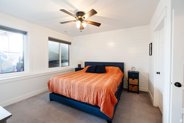 924 Country Lane Farmington, UT 84025 - Photo 57 of 91 Bright bedroom featuring two windows with roller shades, white shiplap accent wall, grey carpeting, and a ceiling fan with integrated lighting