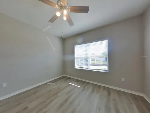 an empty room with wooden floor chandelier fan and windows