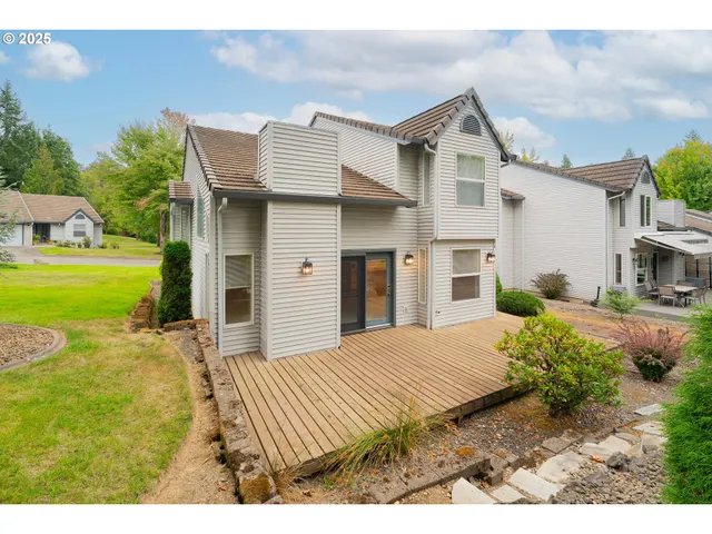 a view of a white house next to a yard with plants and trees