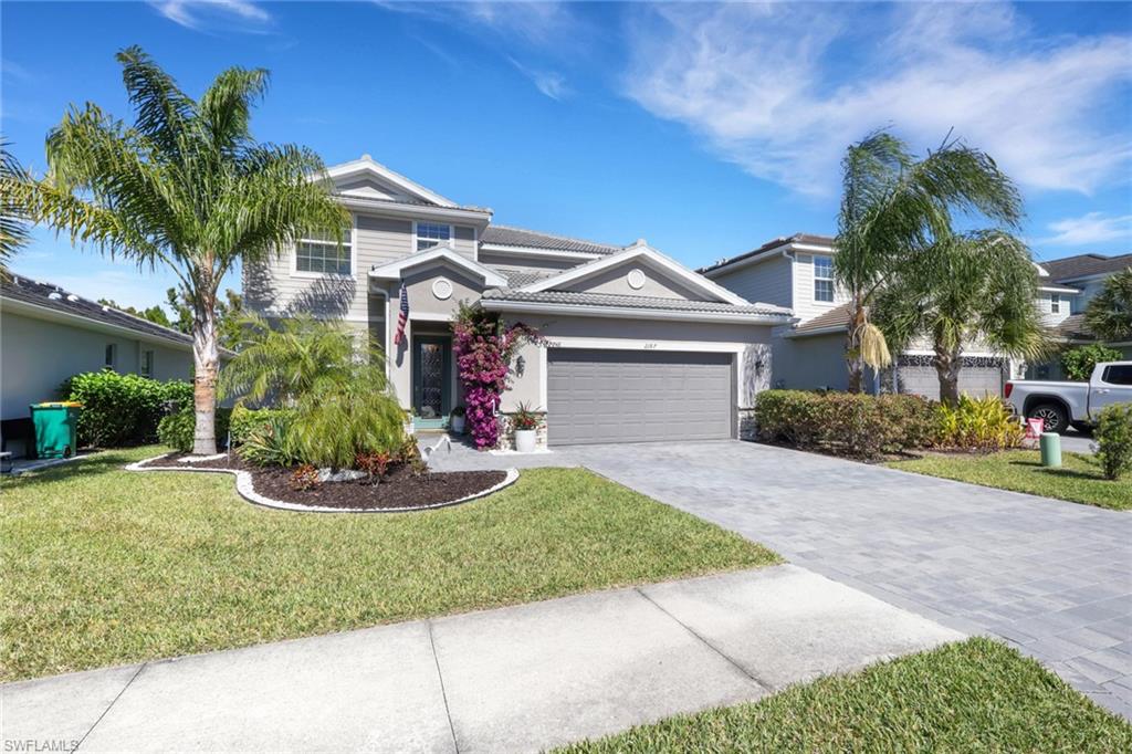 View of front of house featuring a front lawn, decorative driveway, a garage, a tile roof, and stucco siding