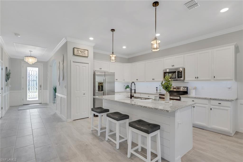 2187 Cara Cara Way Naples, FL 34120 - Photo 3 of 50 Kitchen featuring white cabinets, a kitchen breakfast bar, light stone counters, stainless steel appliances, and a kitchen island with sink