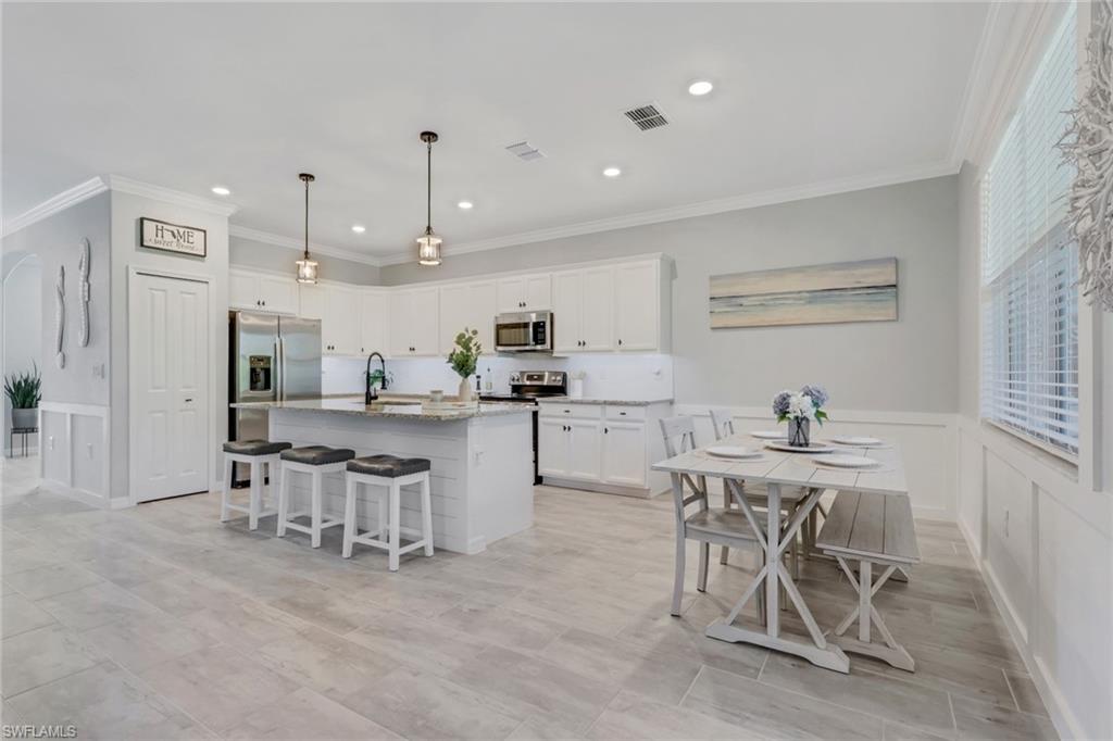 2187 Cara Cara Way Naples, FL 34120 - Photo 5 of 50 Kitchen with a breakfast bar, a kitchen island with sink, white cabinetry, crown molding, and decorative light fixtures