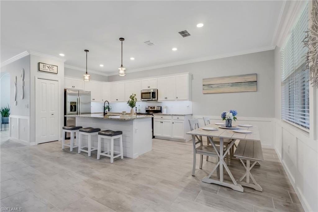 2187 Cara Cara Way Naples, FL 34120 - Photo 7 of 50 Kitchen featuring a wainscoted wall, a breakfast bar, white cabinetry, a center island with sink, and ornamental molding