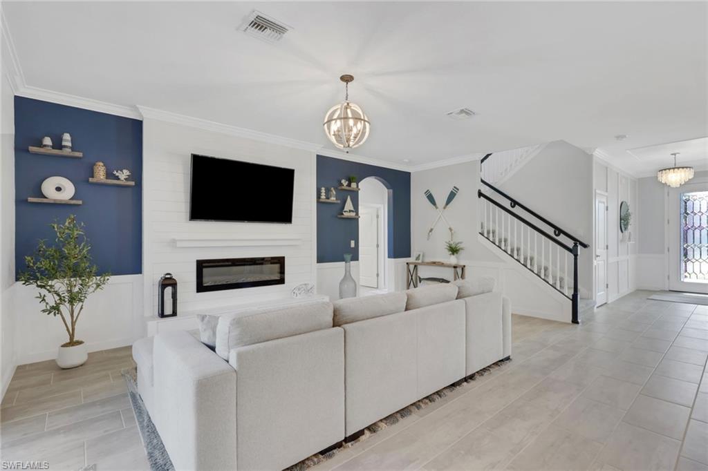2187 Cara Cara Way Naples, FL 34120 - Photo 10 of 50 Living room with suspended lighting, a wainscoted wall, wood finish floors, a fireplace, and arched walkways