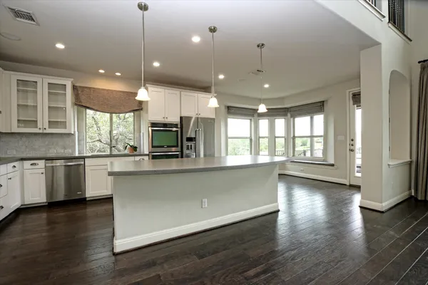 a large kitchen with granite countertop a large kitchen island a sink a stove and wooden floors
