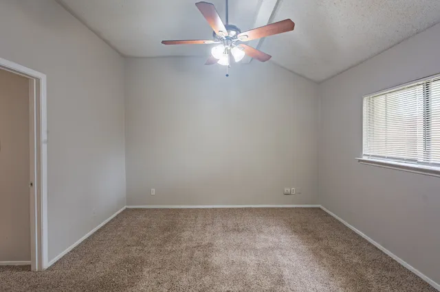an empty room with a chandelier fan and windows