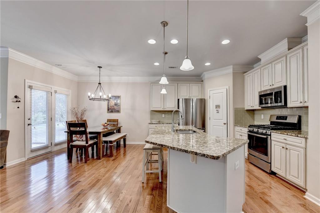 2455 Matlin Way Buford, GA 30519 - Photo 22 of 58 a large kitchen with kitchen island granite countertop a stove a sink a dining table and chairs with wooden floor