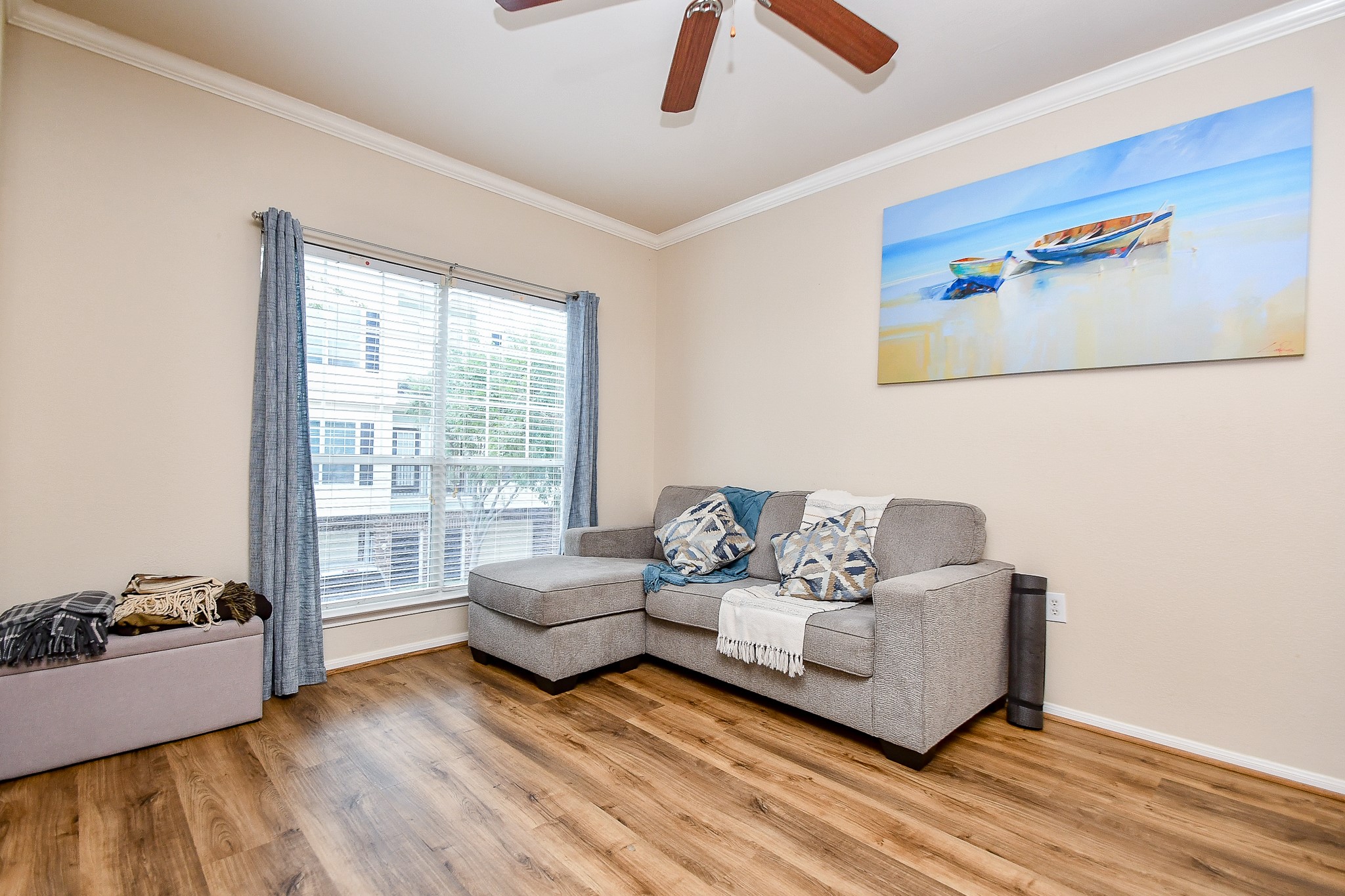 9200 Westheimer Road, Unit 1302 Houston, TX 77063 - Photo 14 of 29 Bright and inviting living room with hardwood floors, a large window providing natural light, The space is enhanced by a ceiling fan and wall art, offering a comfortable setting for relaxation.