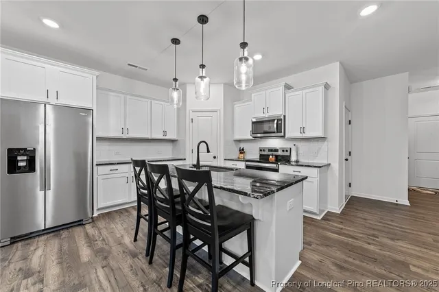 a kitchen with stainless steel appliances granite countertop a table chairs a refrigerator and a stove top oven