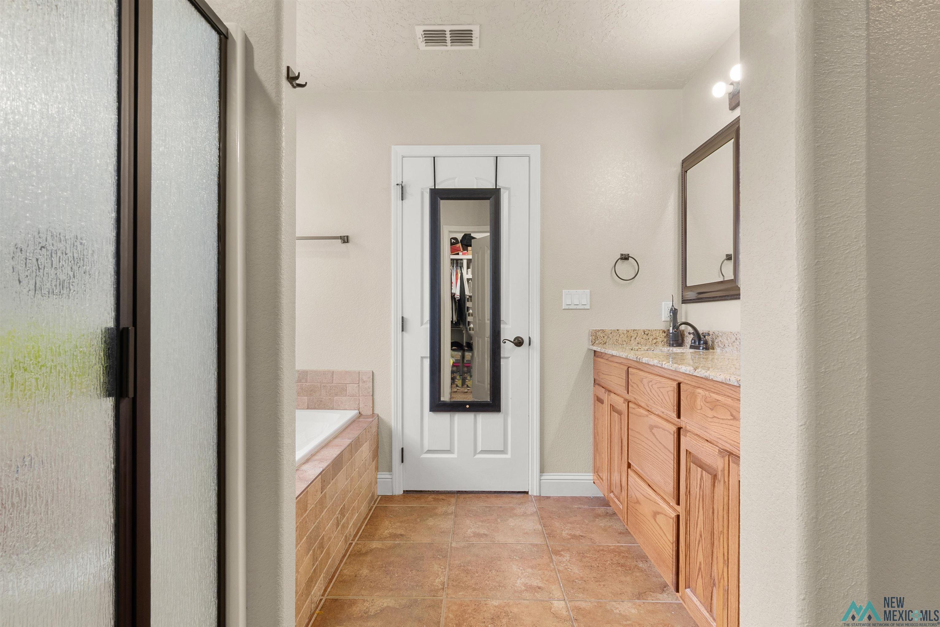 3913 Woodlark Road Clovis, NM 88101 - Photo 20 of 28 Spacious bathroom featuring a shower with a dark framed glass enclosure, a built-in tub with tile surround, a single vanity with wood cabinetry, a light-colored countertop, and a dark framed mirror