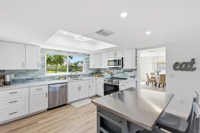 a kitchen with stainless steel appliances granite countertop a stove top oven a sink dishwasher a dining table and chairs with wooden floor