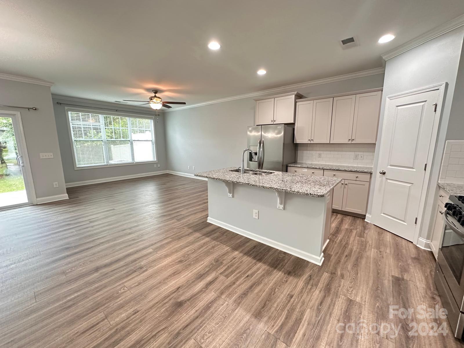 7040 Harris Bay Road Charlotte, NC 28269 - Photo 6 of 27 a large kitchen with granite countertop a stove a sink white cabinets and wooden floor next to a window