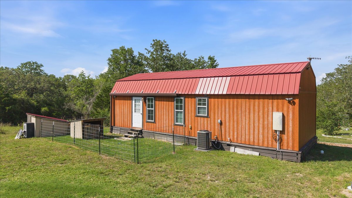 1705 Makinson Road West Point, TX 78963 - Photo 27 of 40 A charming wood-sided residence featuring a vibrant red metal roof and surrounding green expanse.